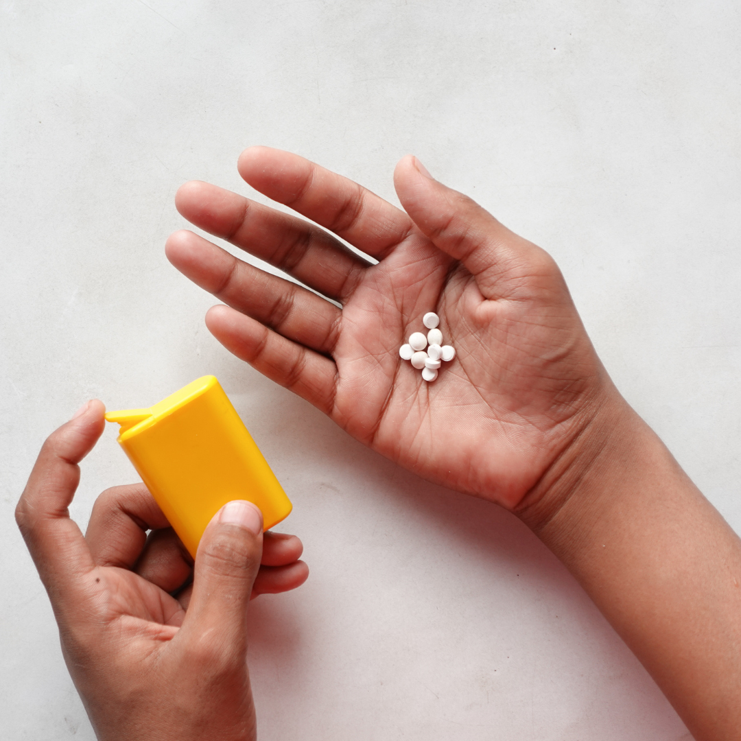 Hand holding a yellow dispenser and white artificial sweetener pills, depicting the choice between natural and synthetic sweetness.