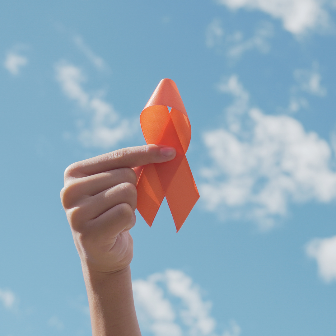 Hand holding an orange ribbon against a blue sky, symbolizing Multiple Sclerosis awareness