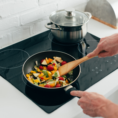 A person cooking a colourful vegetable stir-fry on a stovetop, promoting healthy home-cooked meals.